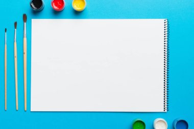 Albüm sayfaları, boyalar, kalemler, renkli arka planda fırçalar. Boşluğu olan üst görünüm. Yaratıcılık için işyeri. ev öğretmenliği kavramı çizimi.