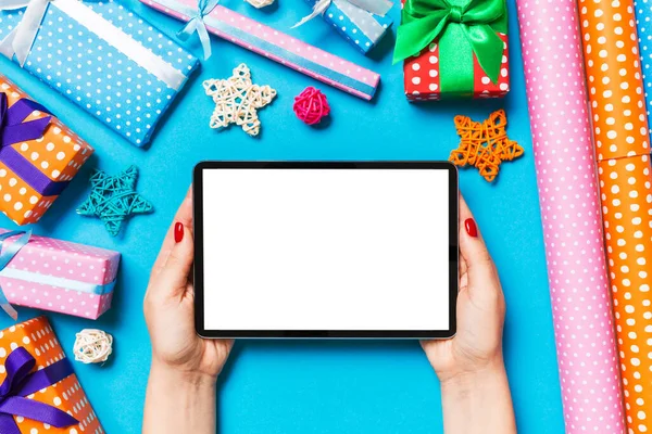 Top view of woman holding tablet in her hands on blue background made of Christmas decorations. New Year holiday concept. Mockup.