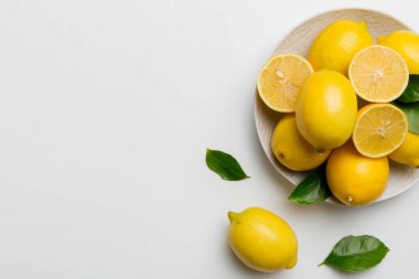 Taze kesilmiş limon ve tüm limonları renkli arka planda yuvarlak tabakta. Yemek ve içecek malzemeleri hazırlanıyor. Sağlıklı beslenme teması üst görünüm kopyalama alanı.