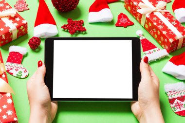 Elinde tabletle Noel süslemelerinden yapılmış yeşil arka planda gezen kadının üst görüntüsü. Yeni yıl tatili konsepti. Model.