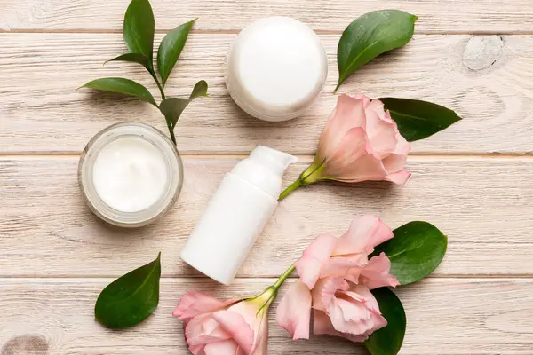 Composition with cosmetic products and beautiful roses on wooden background. Flat lay.