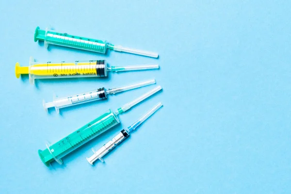 Top view of medical syringes with needles at blue background with copy space. Injection treatment concept.
