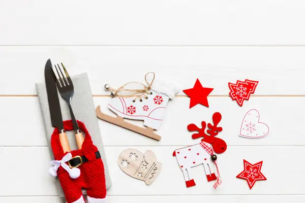 Top view of New Year dinner on wooden background. Festive cutlery on napkin with christmas decorations and toys. Family holiday concept with copy space.