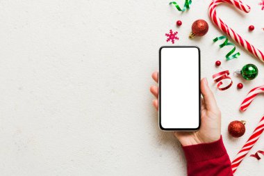 Mesaj atmak için yeri olan bir Noel modeli. Noel reklamı, uygulama şablonu. Masa arkasında boş ekran olan el ele tutuşan telefon. Mutlu yıllar ve Xmas Flat.