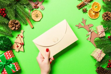 Elinde tatil süslemelerinden yapılmış yeşil arka planda bir zarf tutan kadının üst görüntüsü. Noel zamanı konsepti.