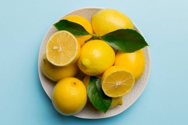 Taze kesilmiş limon ve tüm limonları renkli arka planda yuvarlak tabakta. Yemek ve içecek malzemeleri hazırlanıyor. Sağlıklı beslenme teması üst görünüm kopyalama alanı.