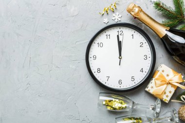 New year celebration concept with a bottle of champagne and two glasses toasting. Christmas gift box, alarm clock and fir tree branch on colored table. Top view Copy space.