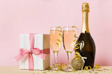 Champagne bottle with confetti, glasses and christmas decor on colored holiday background. Flat lay New Year decorations.