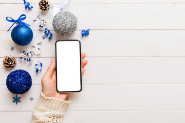 Mesaj atmak için yeri olan bir Noel modeli. Noel reklamı, uygulama şablonu. Masa arkasında boş ekran olan el ele tutuşan telefon. Mutlu yıllar ve Xmas Flat.