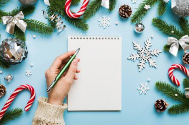 Noel 'i yazmak için bir kadın not defterine Xmas dekorasyonlu renkli arkaplan çiziyor.