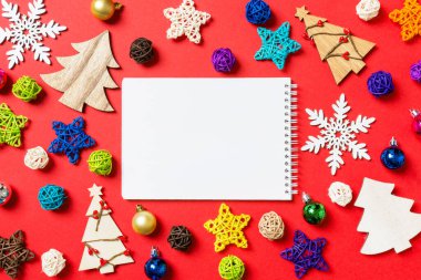 Kırmızı arkaplanda tatil süslemeleri ve oyuncaklardan yapılmış defterin üst görüntüsü. Noel süsü konsepti.