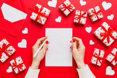 top view photo of valentine day decor female hands holding letter with envelope, small gift box and heart decoration on isolated pastel colored background with empty space.