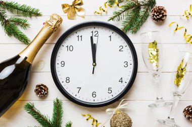 New year celebration concept with a bottle of champagne and two glasses toasting. Christmas gift box, alarm clock and fir tree branch on colored table. Top view Copy space.