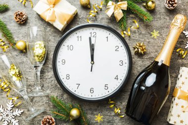 New year celebration concept with a bottle of champagne and two glasses toasting. Christmas gift box, alarm clock and fir tree branch on colored table. Top view Copy space.