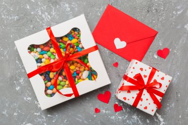 Red envelope with candy and gift box and Valentines hearts on colored background. Flat lay, top view. Romantic love letter for Holiday concept.