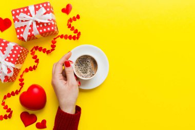 Flat lay of heart shaped cup of black coffee in the hands of women on colored background with copy space top view. Valentine day and holiday concept.