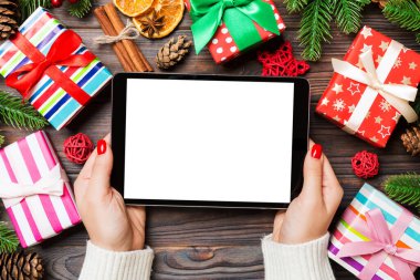 Kadın ellerinin, köknar ağacı ve şenlikli süslemelerden yapılmış ahşap Noel arka planında bir tablet taşıdığı en üst görüntü. Yeni yıl tatili konsepti. Model.