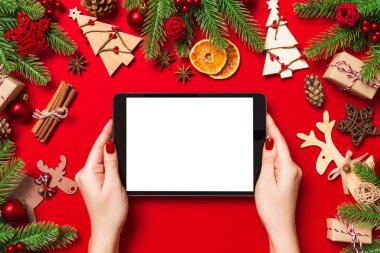 Elinde tabletle Noel süslemelerinden yapılmış kırmızı arka planda duran kadının üst görüntüsü. Yeni yıl tatili konsepti. Model.