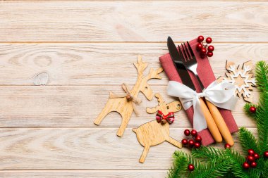 Tahta arka plandaki tatil eşyalarının üst görüntüsü. Utensiller peçeteye kurdele ile bağlanmış. Noel süsleri ve fotokopi alanı olan ren geyikleri. Yeni yıl yemeği konsepti.