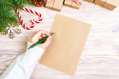 Kız el ahşap arka plan üzerinde süslemeleri ile Kraft kağıt üzerinde Noel mektup yazma.