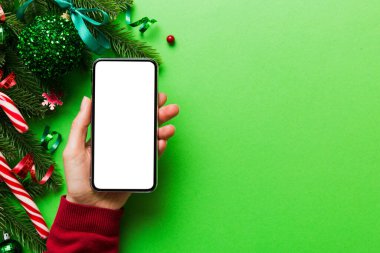 Mesaj atmak için yeri olan bir Noel modeli. Noel reklamı, uygulama şablonu. Masa arkasında boş ekran olan el ele tutuşan telefon. Mutlu yıllar ve Xmas Flat.