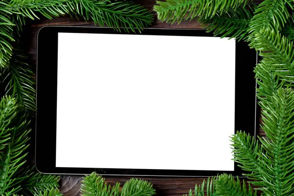 Top view of tablet decorated with a frame made of fir tree on wooden background. New Year time concept.