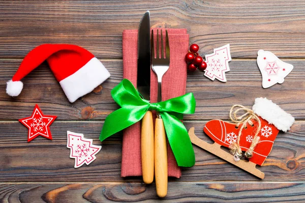 Top view of New Year dinner on wooden background. Festive cutlery on napkin with christmas decorations and toys. Close up of family holiday concept.