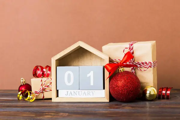 1 january. Christmas composition on colored background with a wooden calendar, with a gift box, toys, bauble copy space.