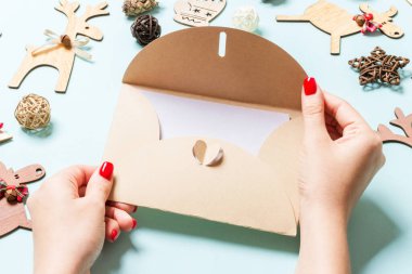 Bayram süslemelerinden yapılmış mavi arka planda bir zarf tutan kadının üst görüntüsü. Noel zamanı konsepti.