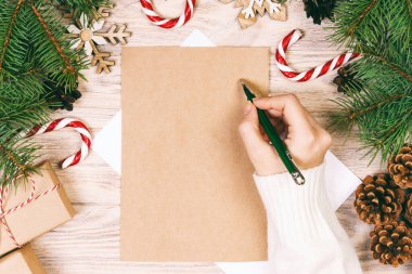 Dişi eller Noel Baba 'ya mektup yazıyor. Noel hediyeleri ve ahşap bir arka planda noel süsü. Yukarıdan bak. Ayarlanmış.