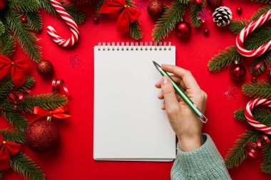 Noel 'i yazmak için bir kadın not defterine Xmas dekorasyonlu renkli arkaplan çiziyor.