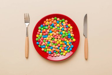 cutlery on table and sweet plate of candy. Health and obesity concept, top view on colored background.