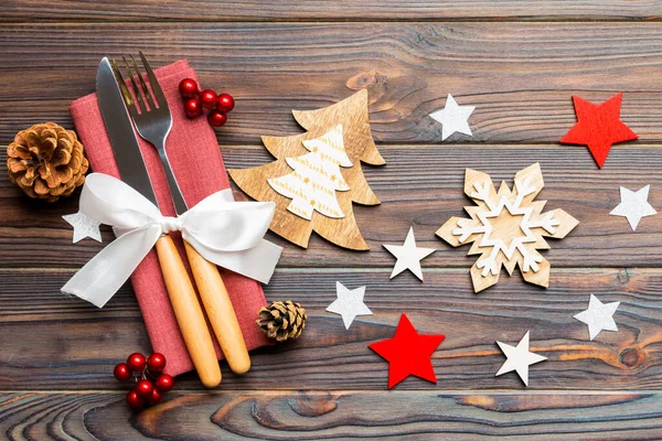 Top view of New Year dinner on wooden background. Festive cutlery on napkin with christmas decorations and toys. Close up of family holiday concept.