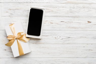Altın kurdeleli hediye kutusu ve arka planda akıllı telefon, üst manzara. Boş kutu paketleme modeli, tasarımınız için şablon - markalaşma modeli.
