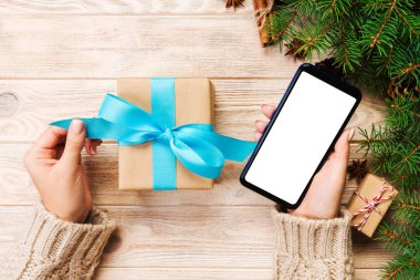 Noel hediye kutusu kaydırma ve telefon masajla mavi şerit kahverengi ahşap masa üzerinde okuma eller basılı tutun. Üstten görünüm.