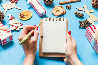 Kadın elinin mavi arka planda notlar alırken üst görüntüsü. Yeni yıl süslemeleri ve oyuncakları. Noel zamanı konsepti.
