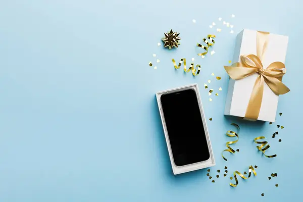 Opened gift box with gold ribbon and smartphone on color background, top view. Blank open box packaging mockup , Template for your design - branding mockup.