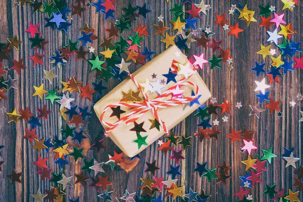 Gift box with star. Creative concept with festive decor on black background. Confetti stars, red, yellow with gift box. Explosion of confetti. Toned.