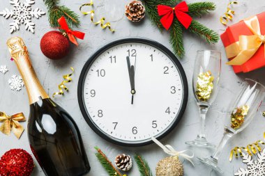 New year celebration concept with a bottle of champagne and two glasses toasting. Christmas gift box, alarm clock and fir tree branch on colored table. Top view Copy space.