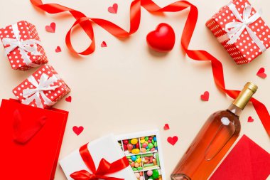 top view photo of st valentine day decor shopping, bag, wine, bottle, envelope, gift, box, candy and red heart on colored background with empty space. Frame background.