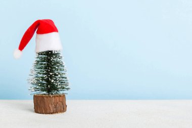 One small Christmas tree with santa hat on colored background. new year decoration with copy space.