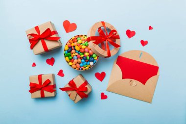 Red envelope with candy and gift box and Valentines hearts on colored background. Flat lay, top view. Romantic love letter for Holiday concept.