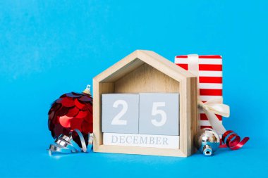 25 december. Christmas composition on colored background with a wooden calendar, with a gift box, toys, bauble copy space.