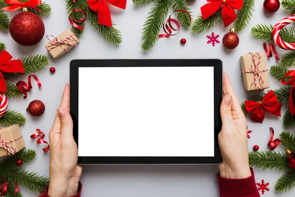 Evden Noel alışverişi, kadın elleri boş beyaz ekranlı tableti tutuyor. Kadın elinde tablet, boş ekran, Noel ağacı ve arka planda hediyeler..