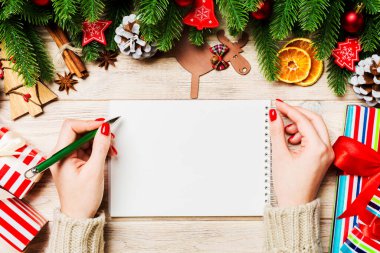 Ahşap Noel arka planında bir not defterine kadın el yazısının üst görüntüsü. Firavun ağacı ve şenlikli süsler. Dilek listesi. Yeni yıl konsepti.