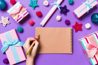 Kadın elinin rengarenk arka planda notlar aldığına dair üst görünüm. Yeni yıl süslemeleri ve oyuncakları. Noel zamanı konsepti.