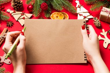 Kadın elinin kırmızı arka planda notlar alırken üst görüntüsü. Yeni yıl süslemeleri ve oyuncakları. Noel zamanı konsepti.