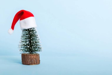 One small Christmas tree with santa hat on colored background. new year decoration with copy space.