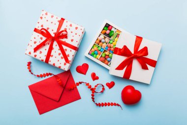 Red envelope with candy and gift box and Valentines hearts on colored background. Flat lay, top view. Romantic love letter for Holiday concept.