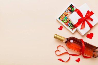 Sevgililer Günü için renkli arka planda bir şişe kırmızı şarap hediye ve çikolatalı. Kalp, hediye kutusuyla şekillendirilmiş çikolatalar fotokopi alanı ile üst görünüm.